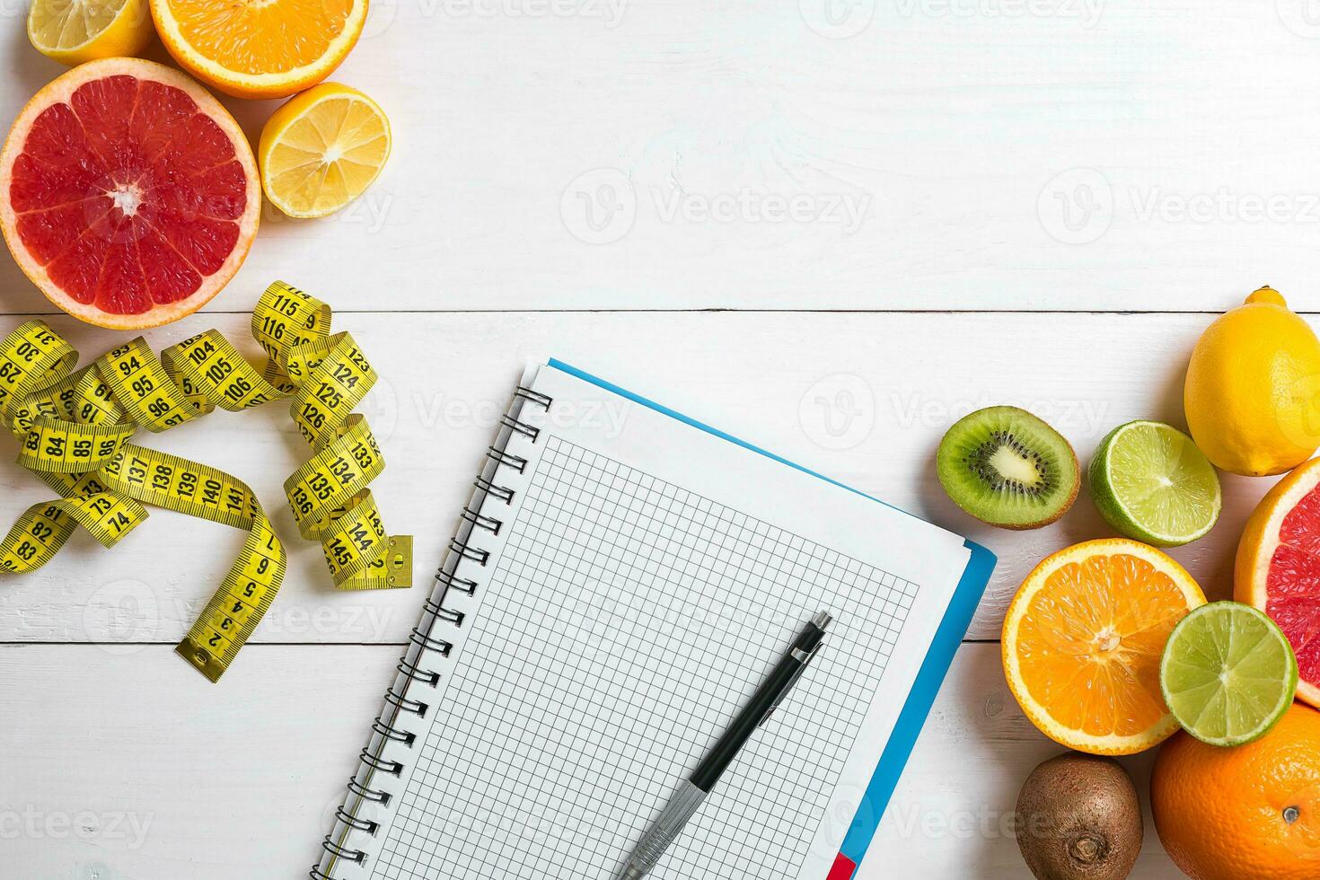 Fresh juice in glass from citrus fruits - lemon, grapefruit, orange, notebook with pencil on white wooden background photo