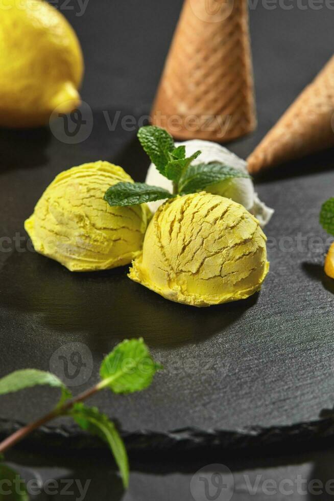 Tasty creamy and lemon ice cream decorated with mint served on a stone slate over a black background. photo