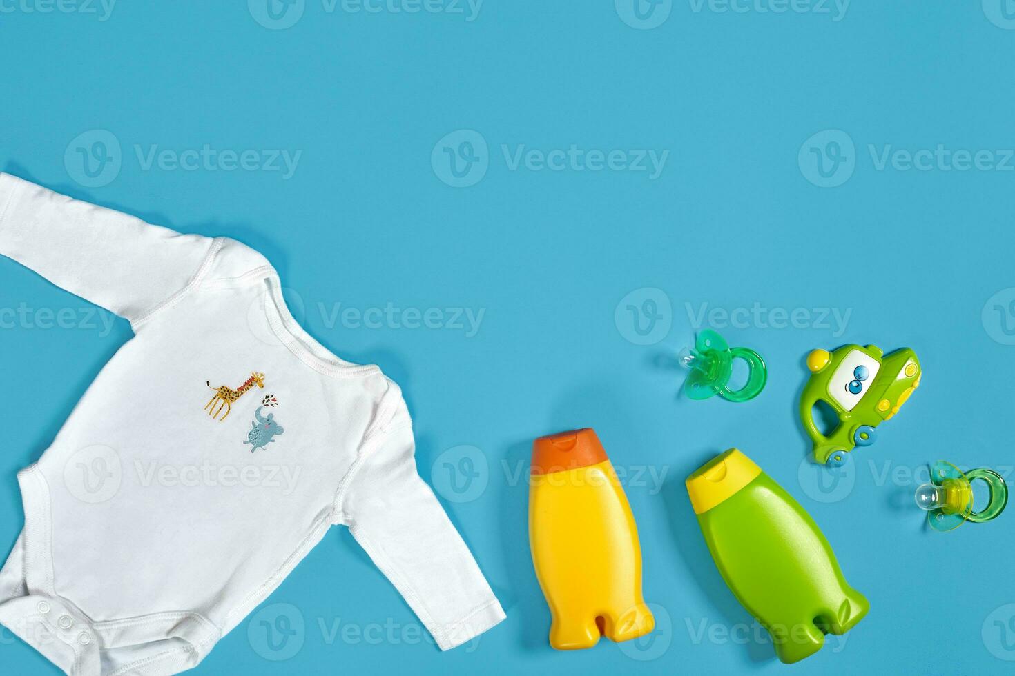 Baby care with bath set. Nipple, toy, clothes, shampoo on blue background top view mockup photo