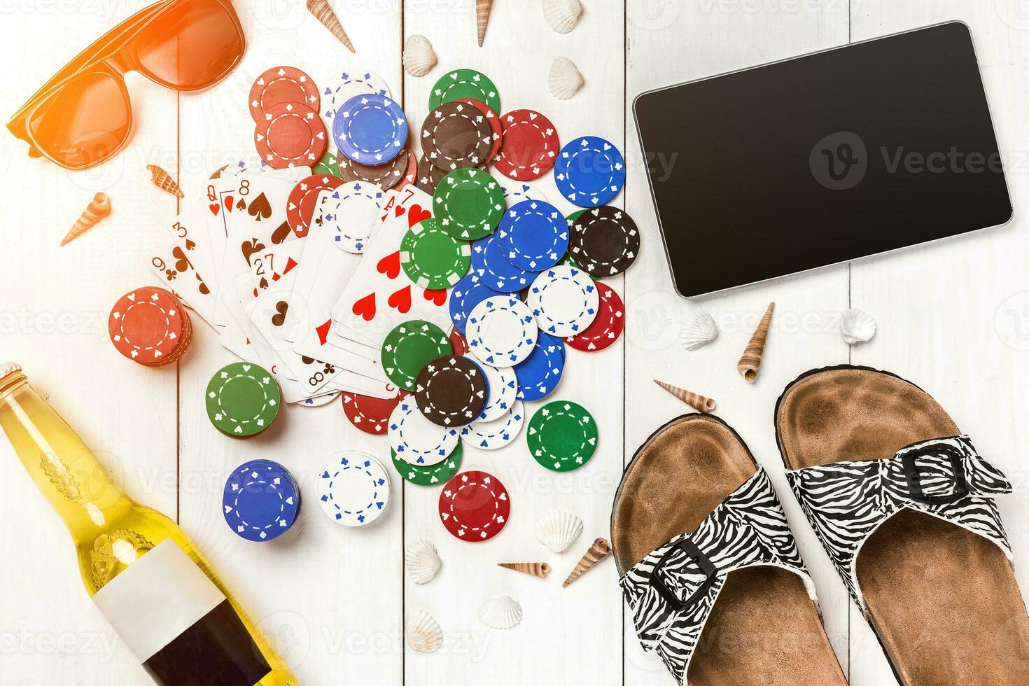 Card deck surrounded by poker chips and scattered seashells on white wooden background with copy space photo