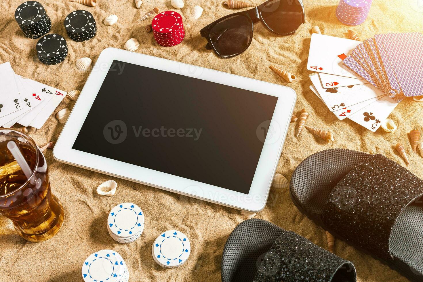 Online poker game on the beach with digital tablet and stacks of chips. Top view photo