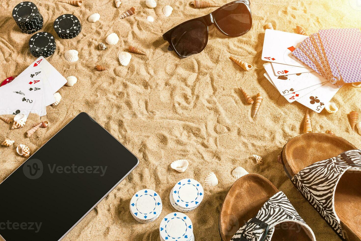 Online poker game on the beach with digital tablet and stacks of chips. Top view photo