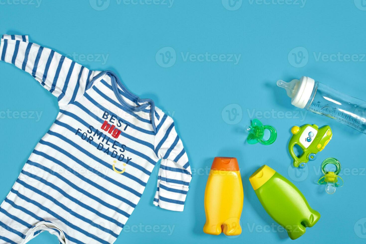 Baby care with bath set. Nipple, toy, clothes, shampoo on blue background top view mockup photo