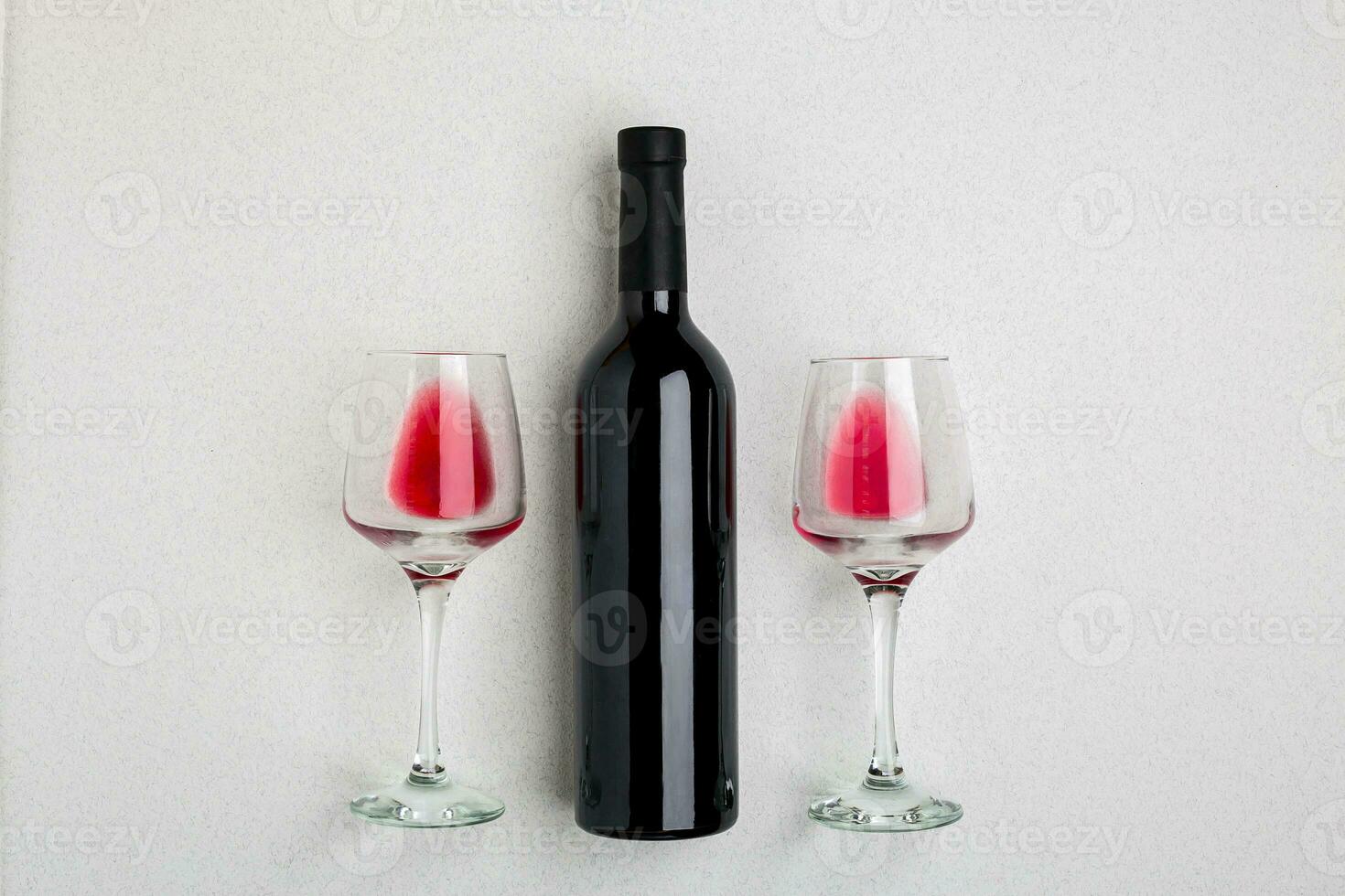 Overhead angled view of a large bottle of red wine, drinking glasses on white background photo