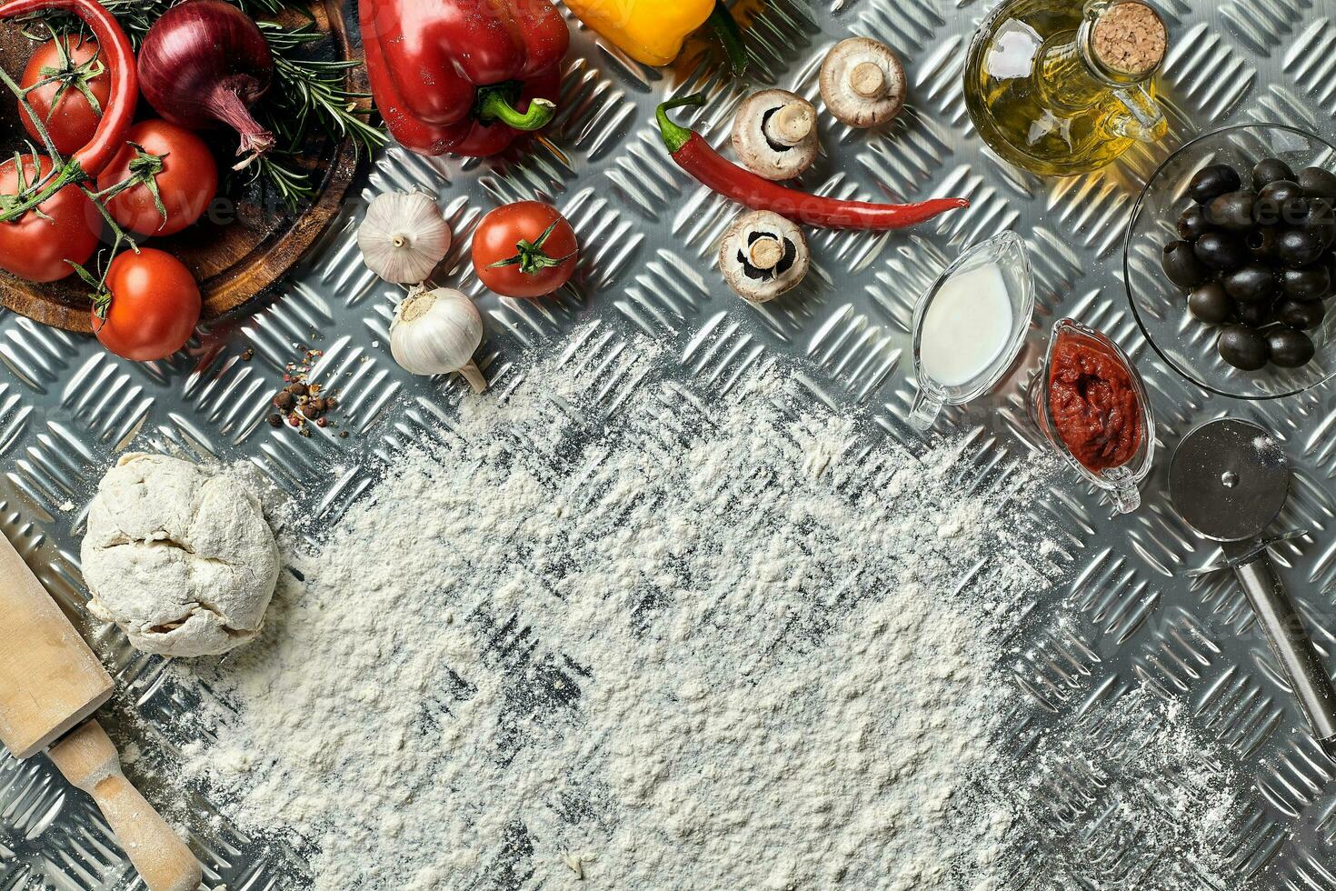 Ingredients and dough for making pizzas with an overhead view on freshly mixed mounds of pastry, a jar of olive oil and pot of tomato sauce, overhead view photo