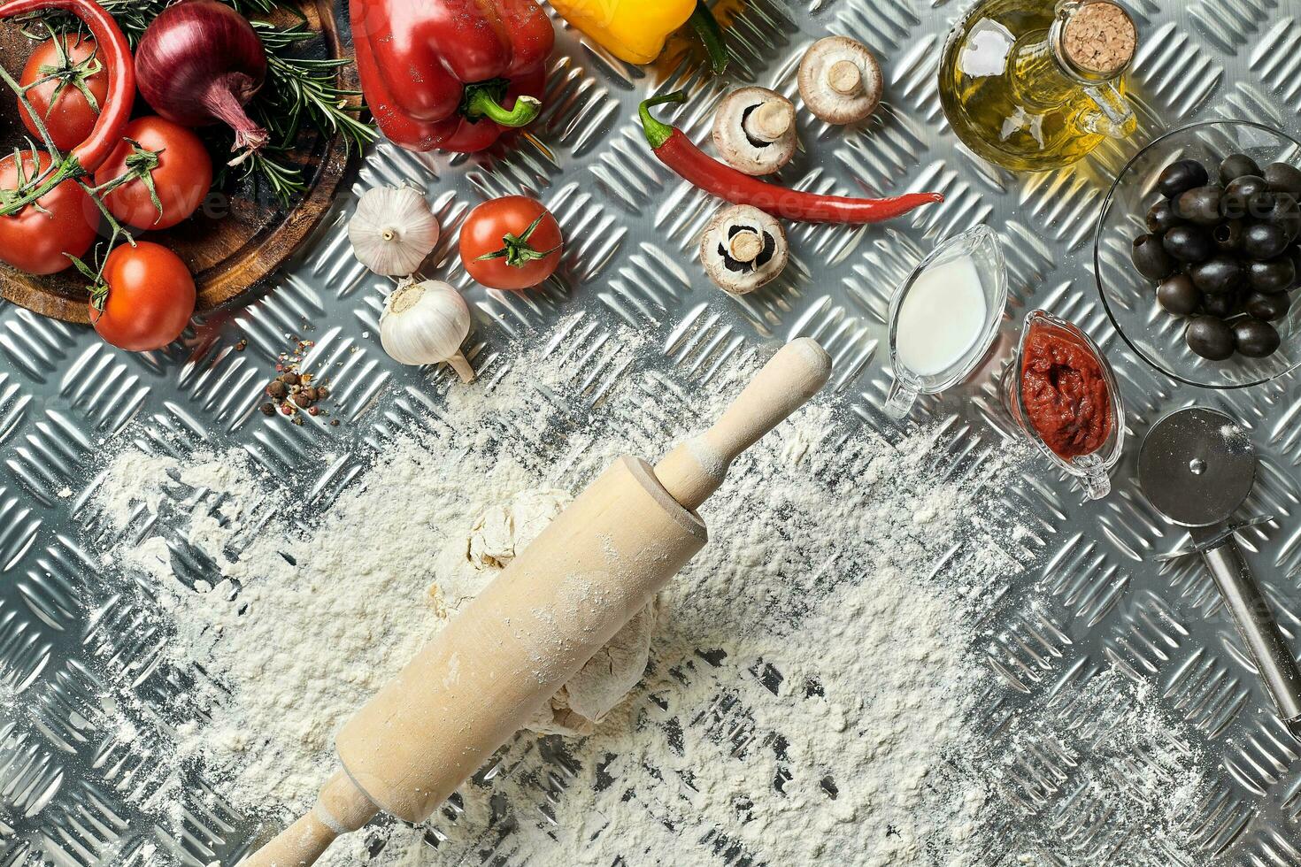 Ingredients and dough for making pizzas with an overhead view on freshly mixed mounds of pastry, a jar of olive oil and pot of tomato sauce, overhead view photo