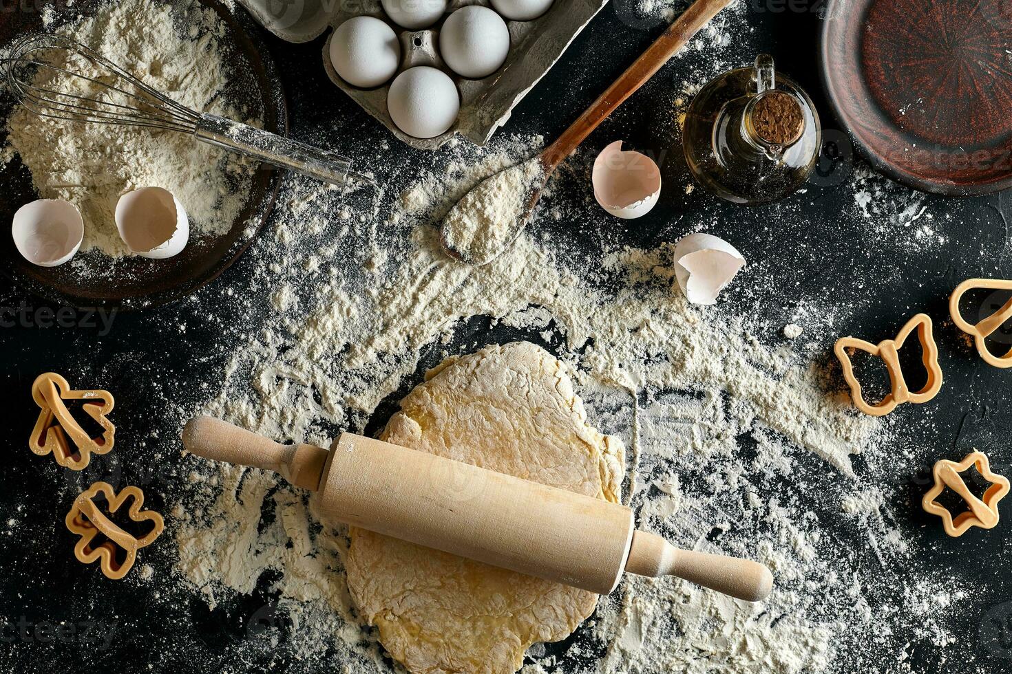 Female hands rolling dough with a rolling pin on a black table. Top view photo