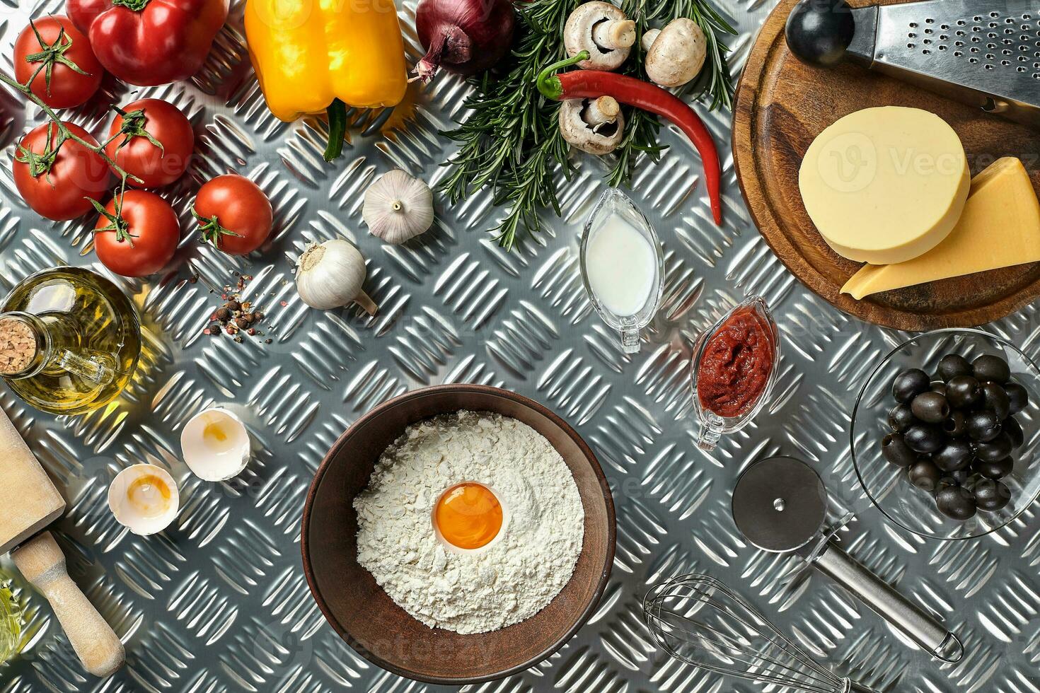 Ingredients and dough for making pizzas with an overhead view on freshly mixed mounds of pastry, a jar of olive oil and pot of tomato sauce, overhead view photo