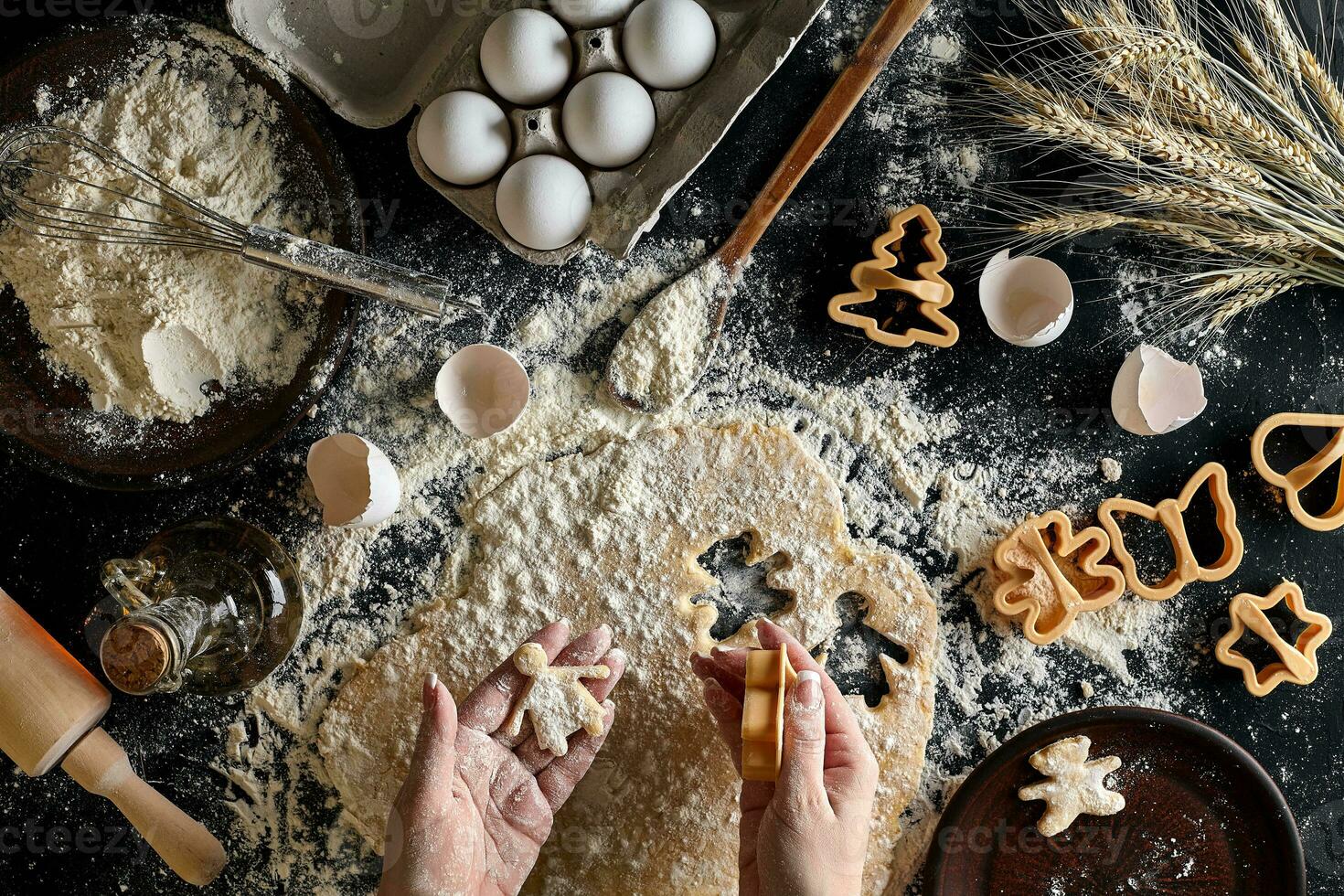 Close-up of a woman's hand with a dough. The woman is cutting a cookie with a cookie cutter in the shape of a little human. View from above. photo