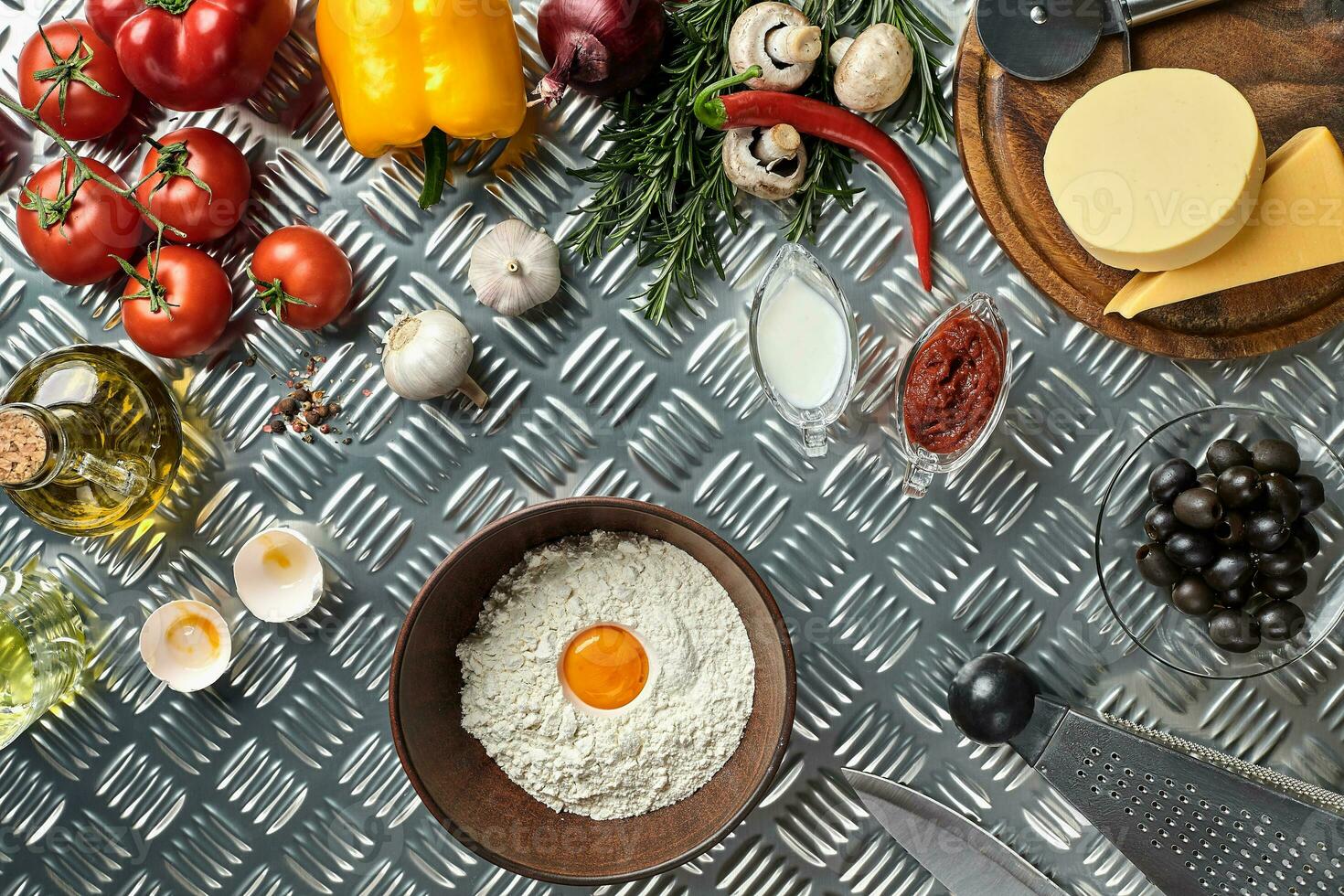 Ingredients and dough for making pizzas with an overhead view on freshly mixed mounds of pastry, a jar of olive oil and pot of tomato sauce, overhead view photo