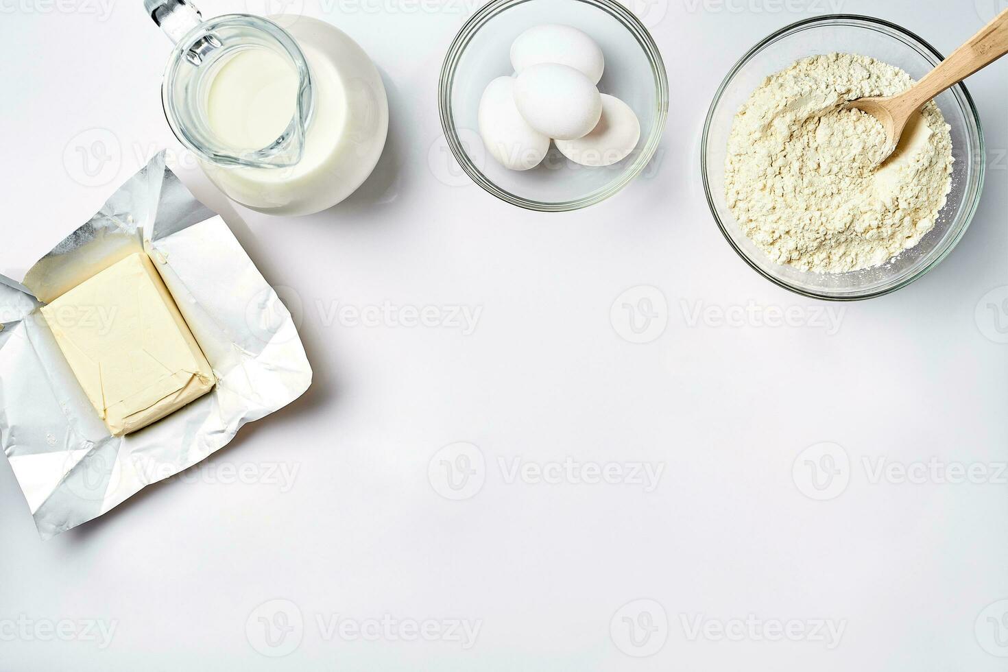 Wheat flour in the glass bowl, cream in a glass jar, butter, chicken eggs - ingredients for the dough, top view photo