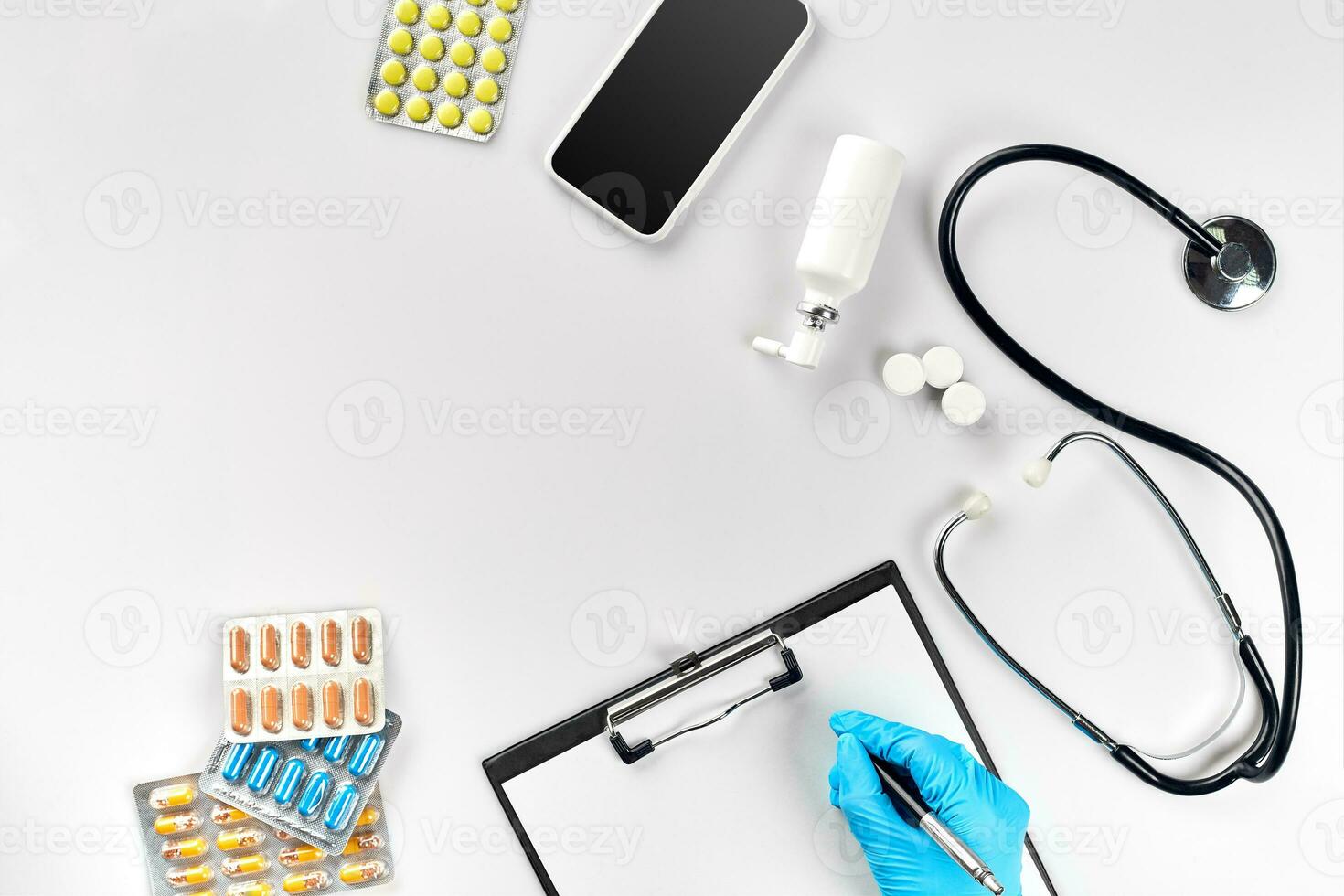 Workplace of a doctor. Pills in hand, stethoscope, clipboard and glasses on white table photo