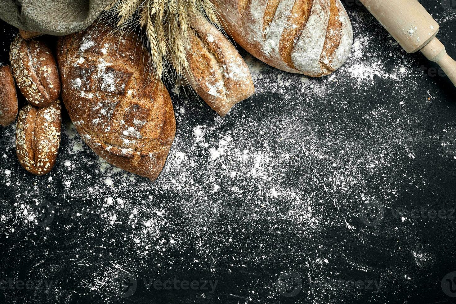 hecho en casa centeno un pan rociado con harina y varios granos y semillas en un negro antecedentes con espiguillas de trigo o centeno y avena. foto