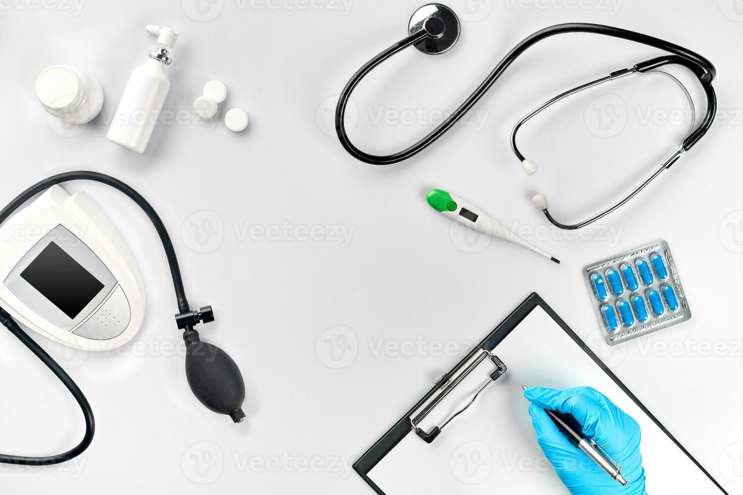 Workplace of a doctor. Pills in hand, stethoscope, clipboard and glasses on white table photo