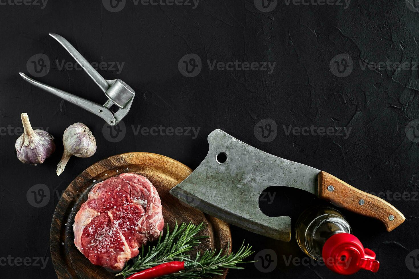Piece of beef tenderloin, with ax for cutting and chopping meat, spices were cooking - rosemary, pepper, salt, garlic. On old wooden board on stone black table. photo