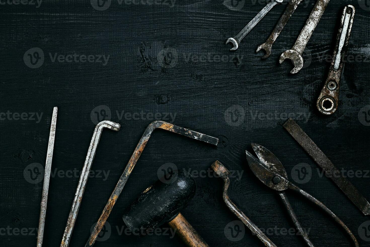 Old, rusty tools lying on a black wooden table. Hammer, chisel, metal scissors, wrench. photo