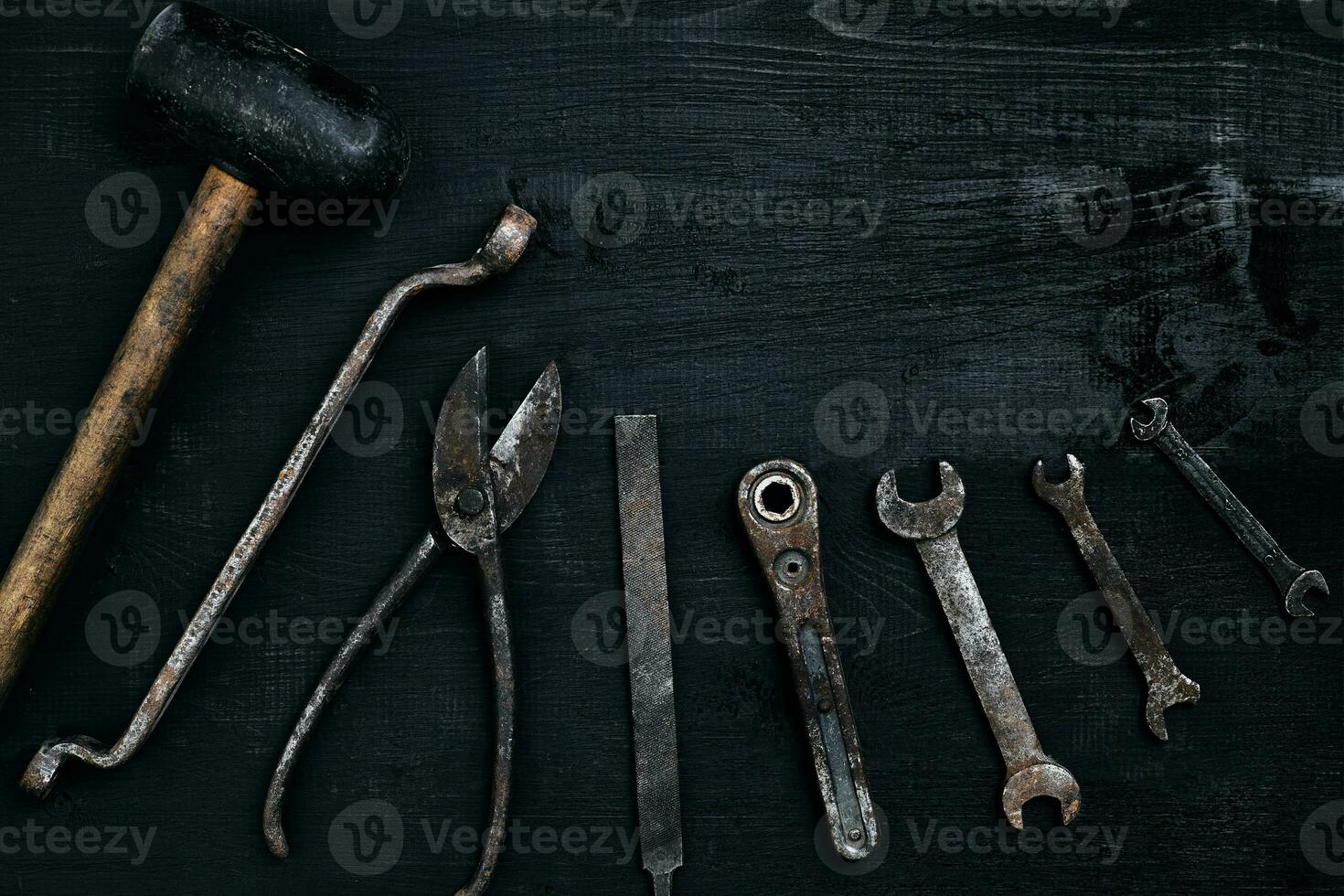 Old, rusty tools lying on a black wooden table. Hammer, chisel, metal scissors, wrench. photo