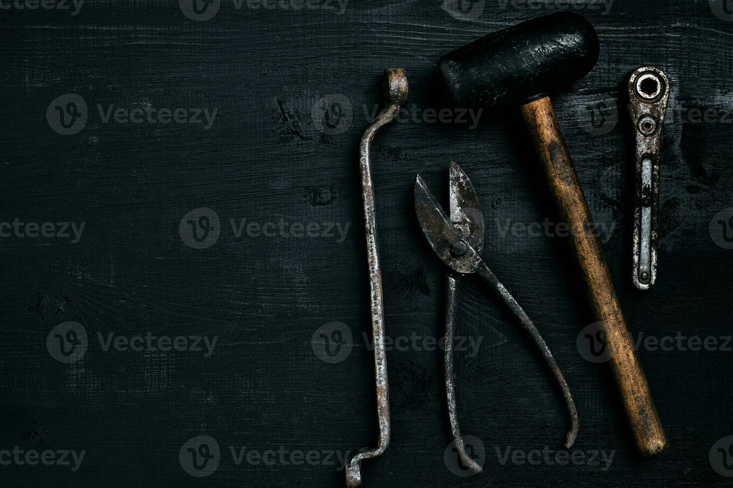 Old, rusty tools lying on a black wooden table. Hammer, chisel, metal scissors, wrench. photo