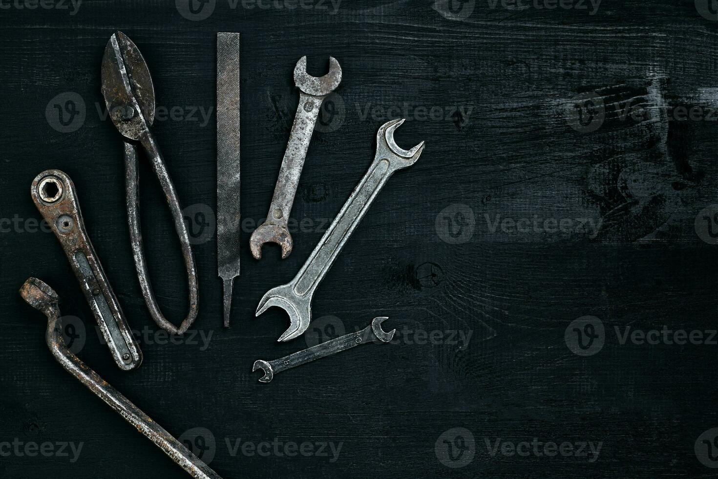 Old, rusty tools lying on a black wooden table. Hammer, chisel, metal scissors, wrench. photo