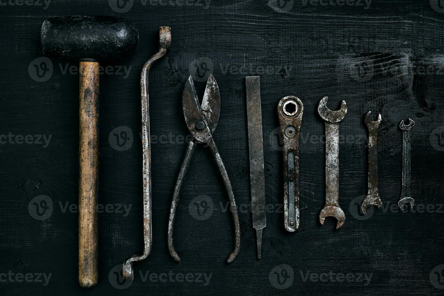 Old, rusty tools lying on a black wooden table. Hammer, chisel, metal scissors, wrench. photo