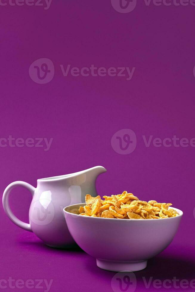 Bowl with corn flakes, jug of milk on purple background. oncept of a healthy breakfast photo