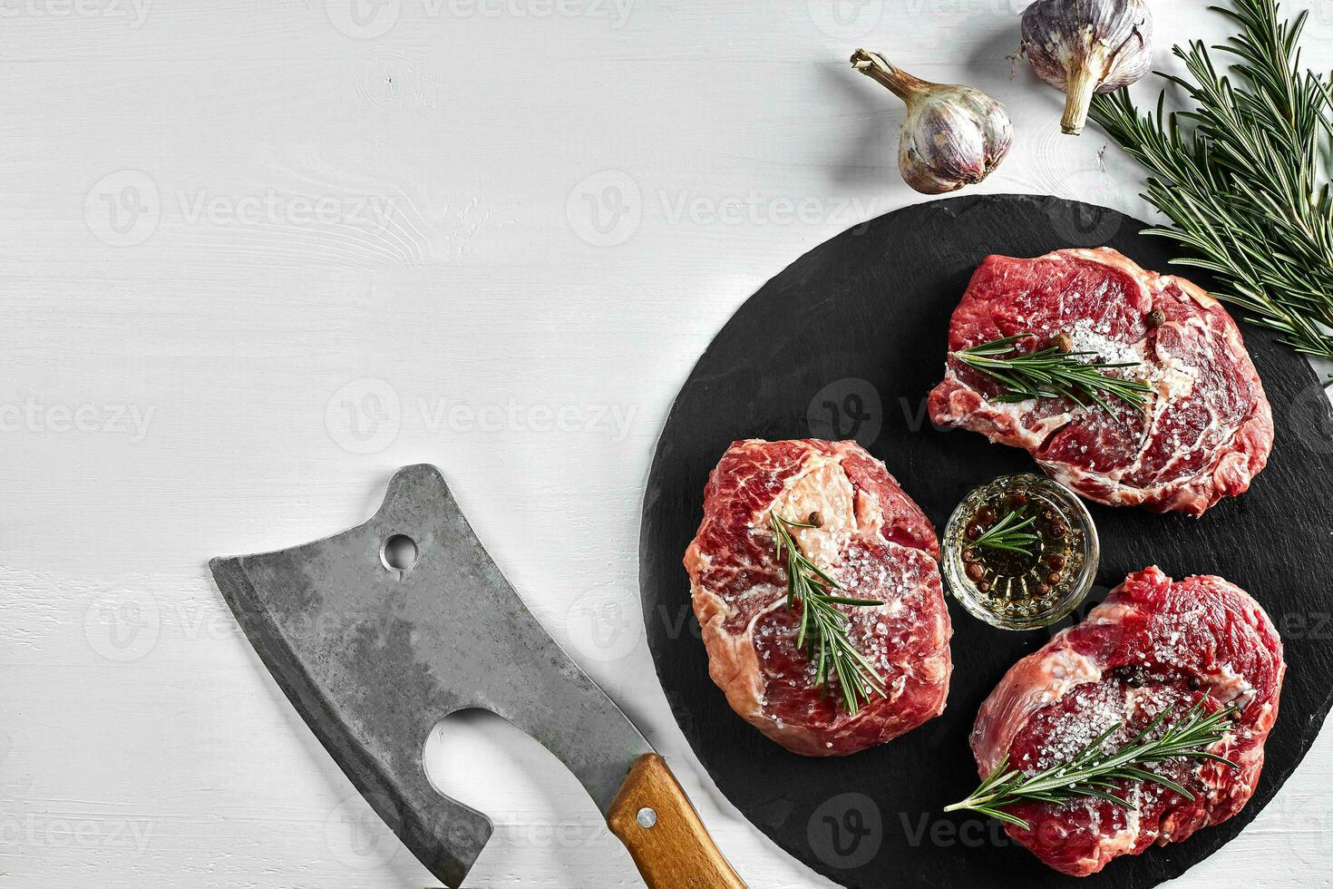 Fresh raw beef steaks with herbs, garlic, olive oil, pepper, salt and rosemary on black board Tenderloin, Striploin, Rib Eye photo