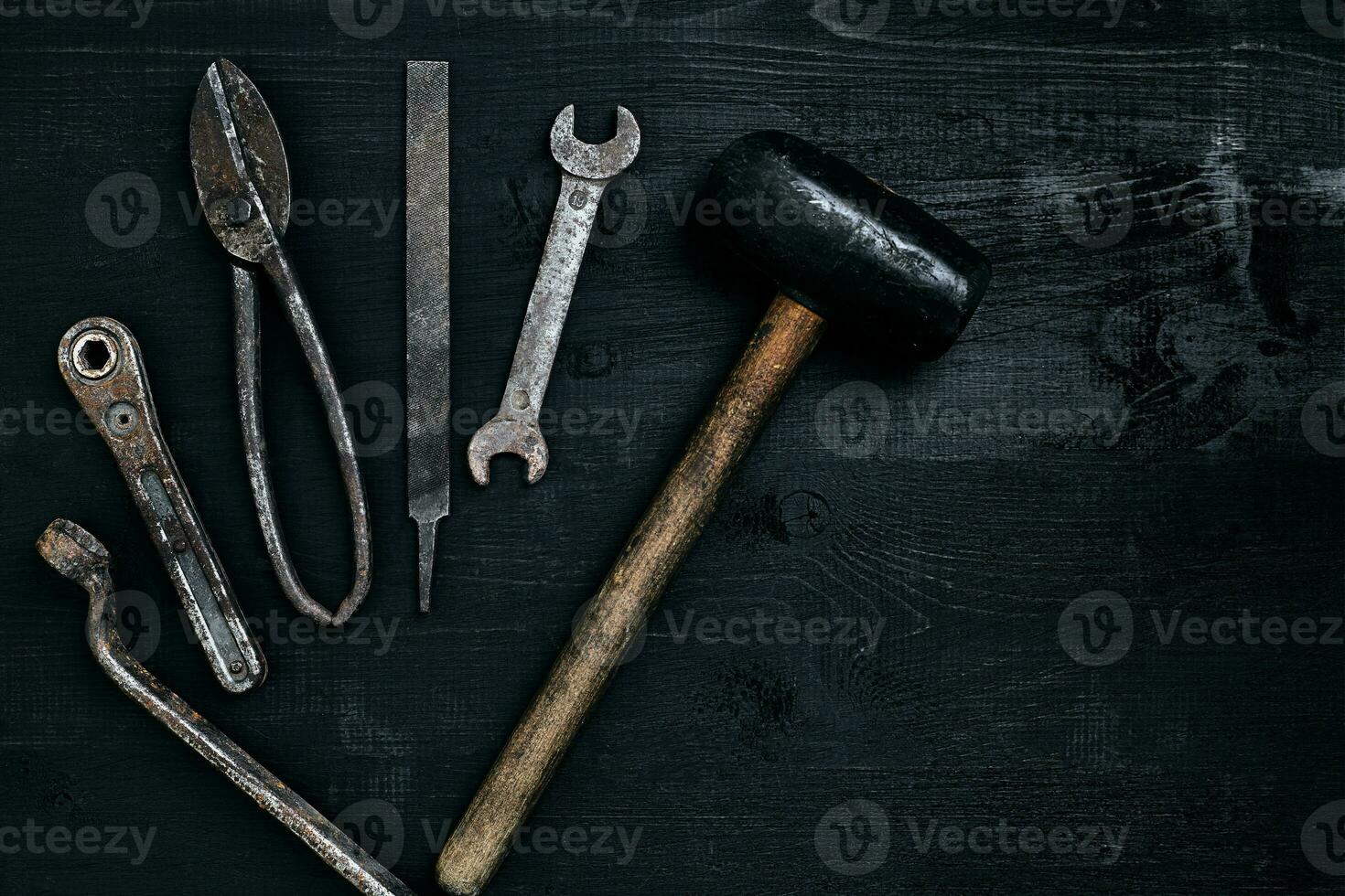 Old, rusty tools lying on a black wooden table. Hammer, chisel, metal scissors, wrench. photo