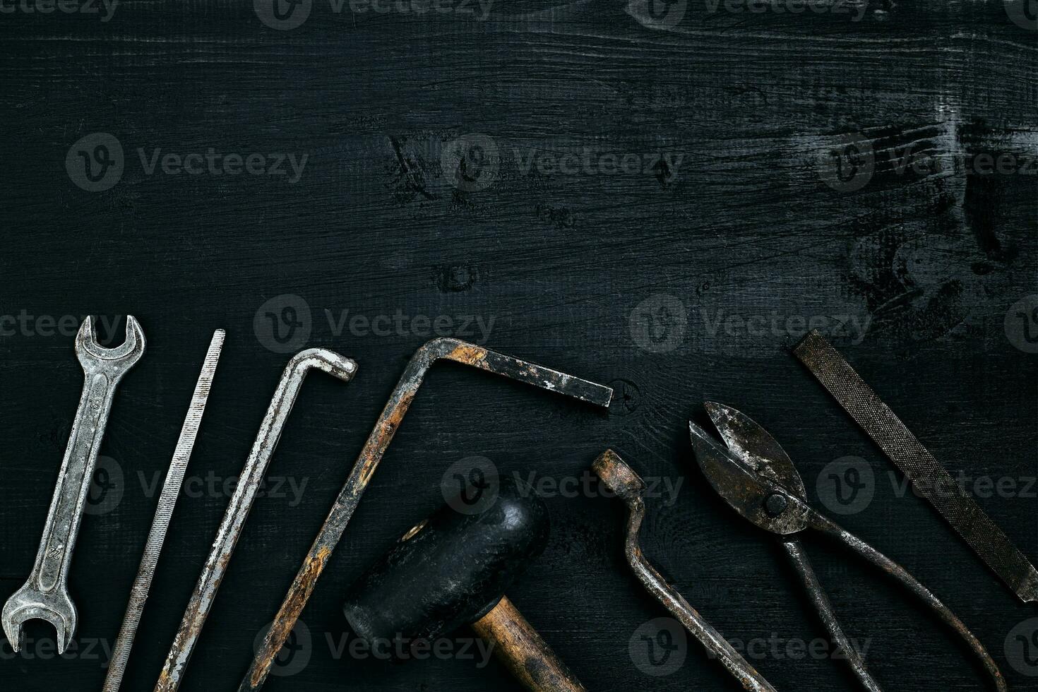 Old, rusty tools lying on a black wooden table. Hammer, chisel, metal scissors, wrench. photo