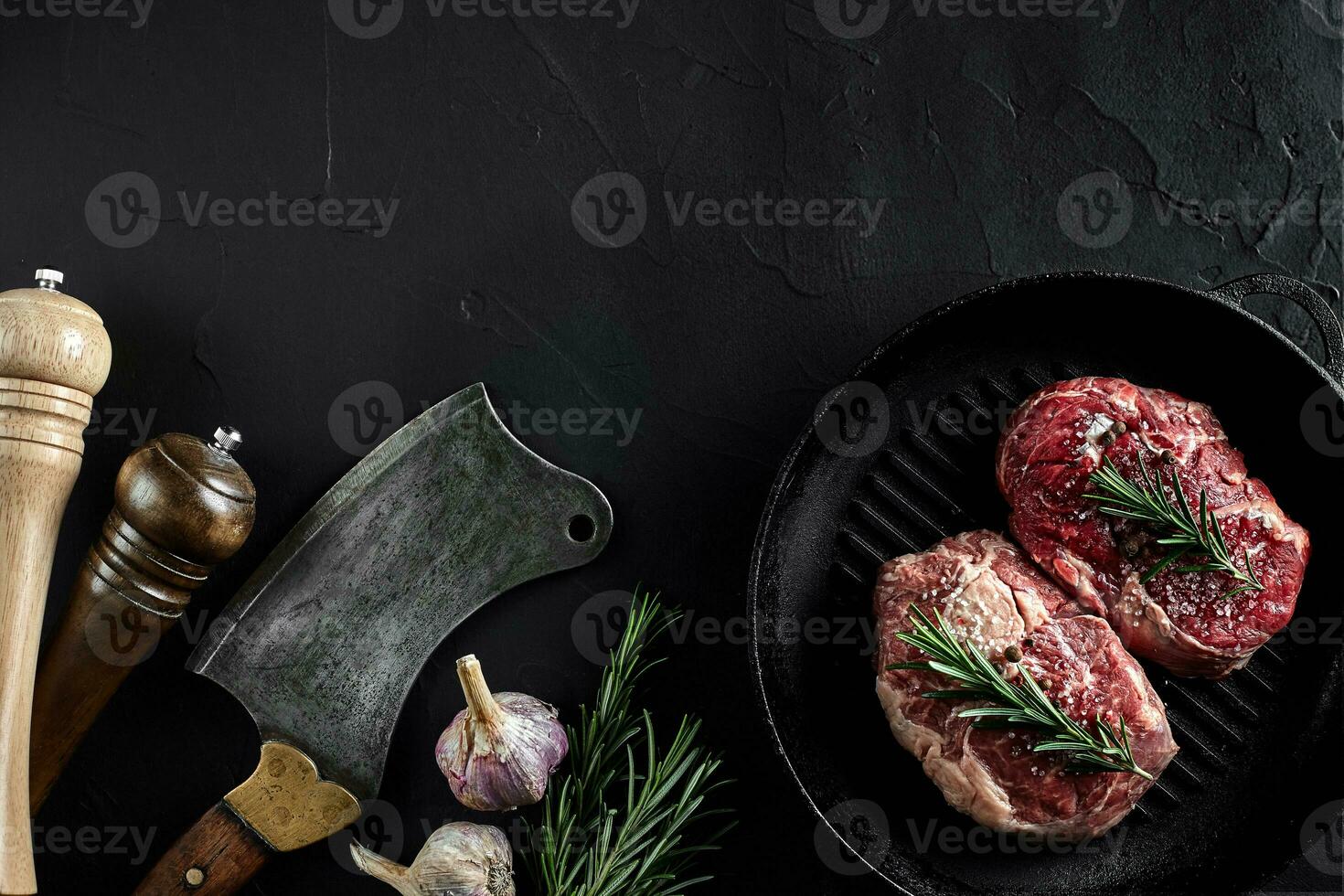 Fresh raw meat. A piece of beef tenderloin on grill pan, with a cutting ax, with spices for cooking on black stone table. Copy space photo