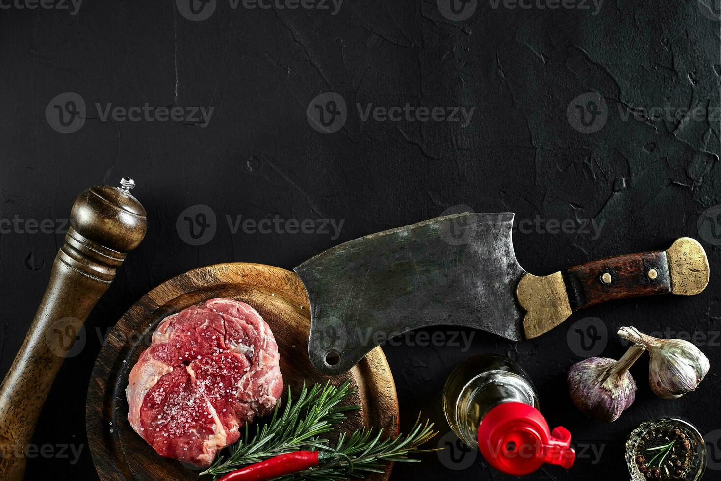 Piece of beef tenderloin, with ax for cutting and chopping meat, spices were cooking - rosemary, pepper, salt, garlic. On old wooden board on stone black table. photo