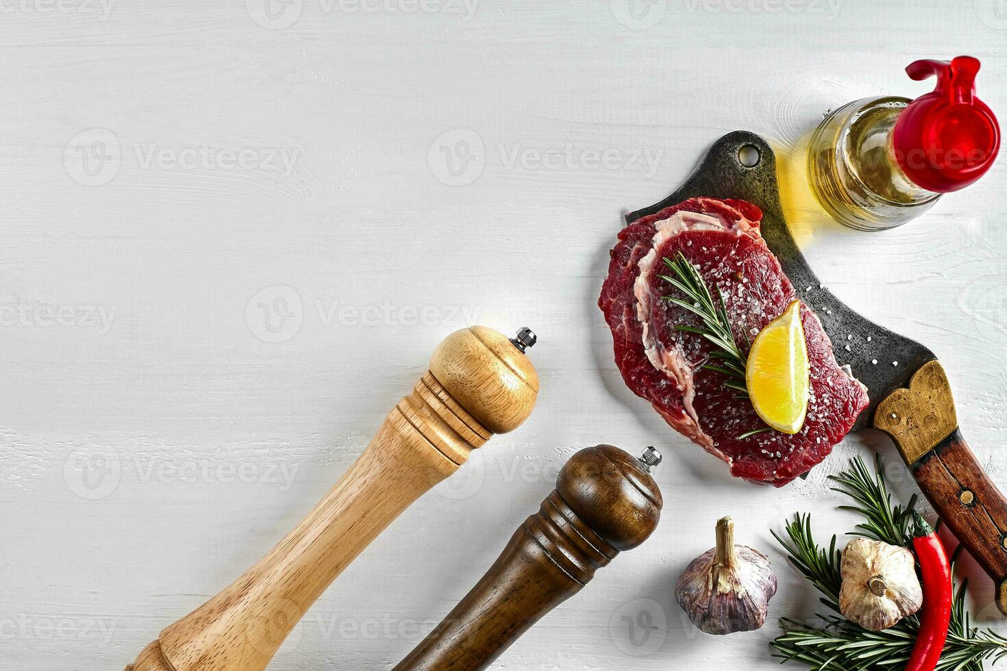 Fresh raw steaks with herbs, garlic, olive oil, pepper, salt, rosemary and a kitchen ax on white background. Top view. photo