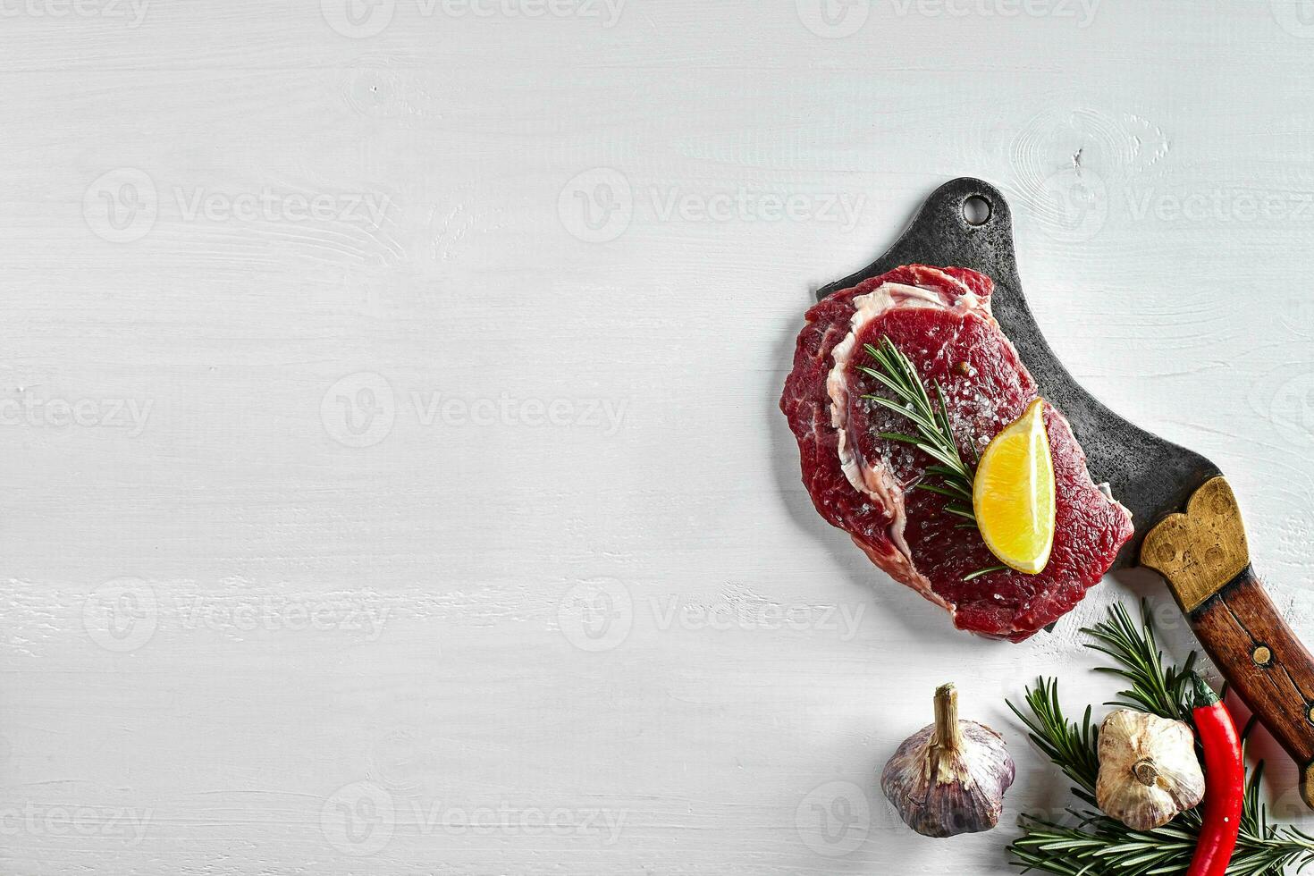 Fresh raw steaks with herbs, garlic, olive oil, pepper, salt, rosemary and a kitchen ax on white background. Top view. photo