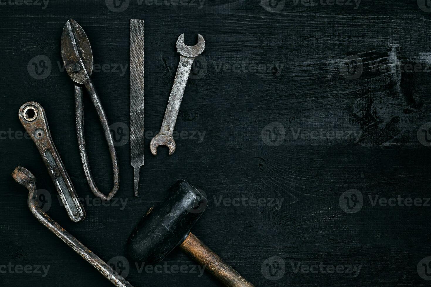 Old, rusty tools lying on a black wooden table. Hammer, chisel, metal scissors, wrench. photo