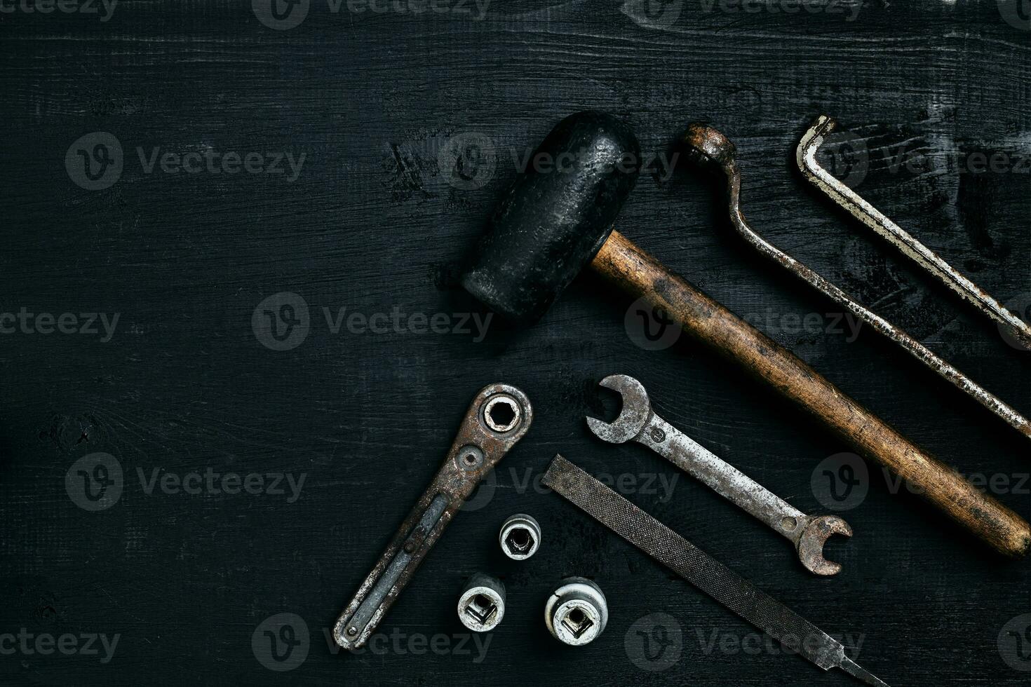 Old, rusty tools lying on a black wooden table. Hammer, chisel, metal scissors, wrench. photo