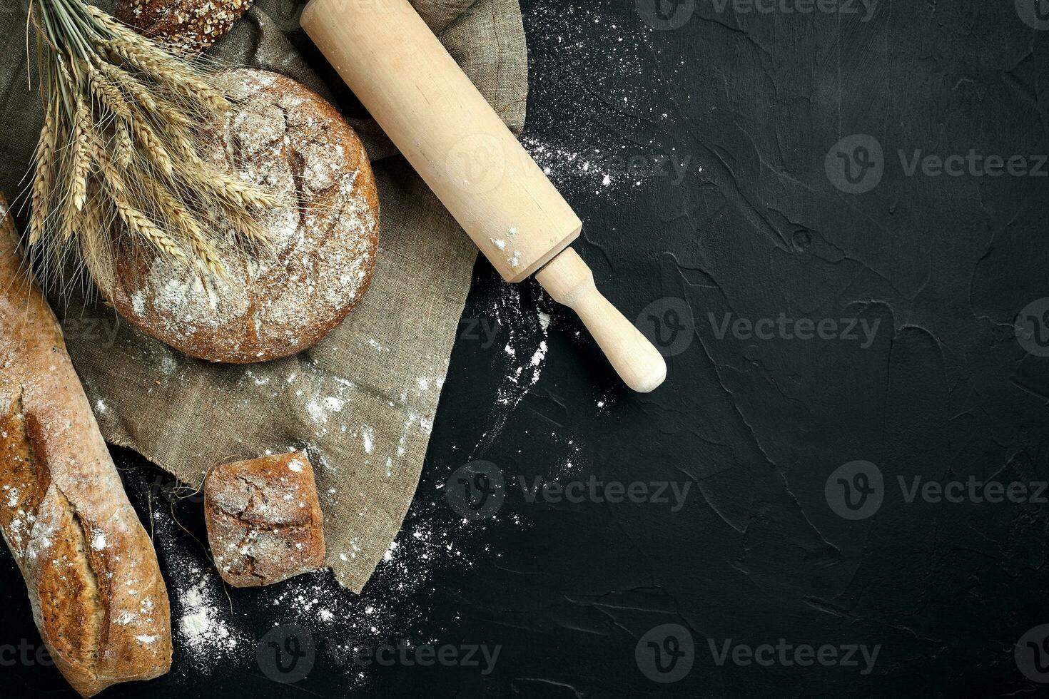 Top view of baguette, baked bread, flour and wheat spikes composition with wheat flour sprinkled around on a dark background photo