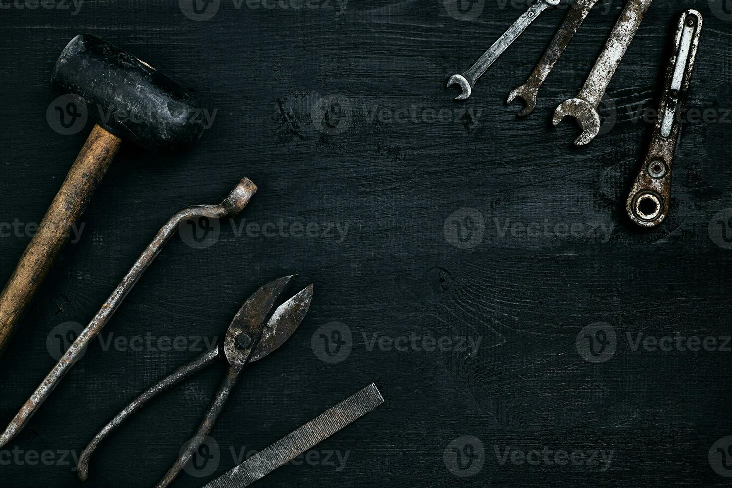 Old, rusty tools lying on a black wooden table. Hammer, chisel, metal scissors, wrench. photo