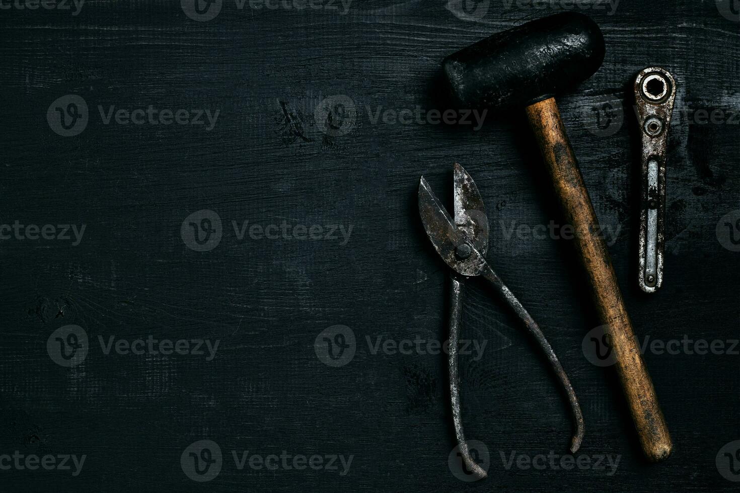 Old, rusty tools lying on a black wooden table. Hammer, chisel, metal scissors, wrench. photo