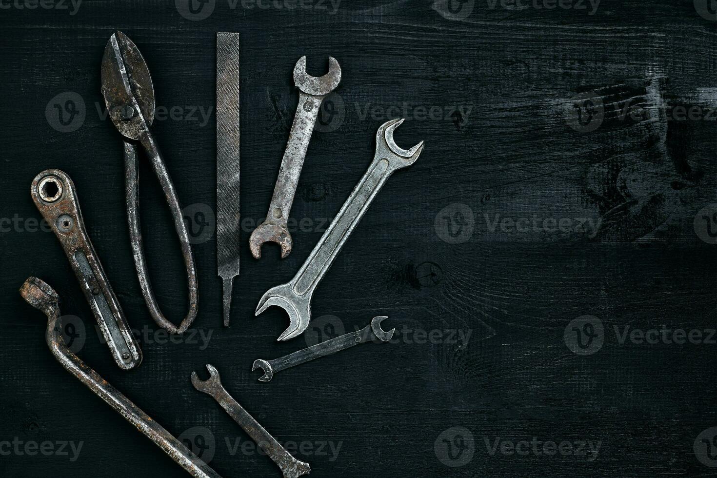 Old, rusty tools lying on a black wooden table. Hammer, chisel, metal scissors, wrench. photo