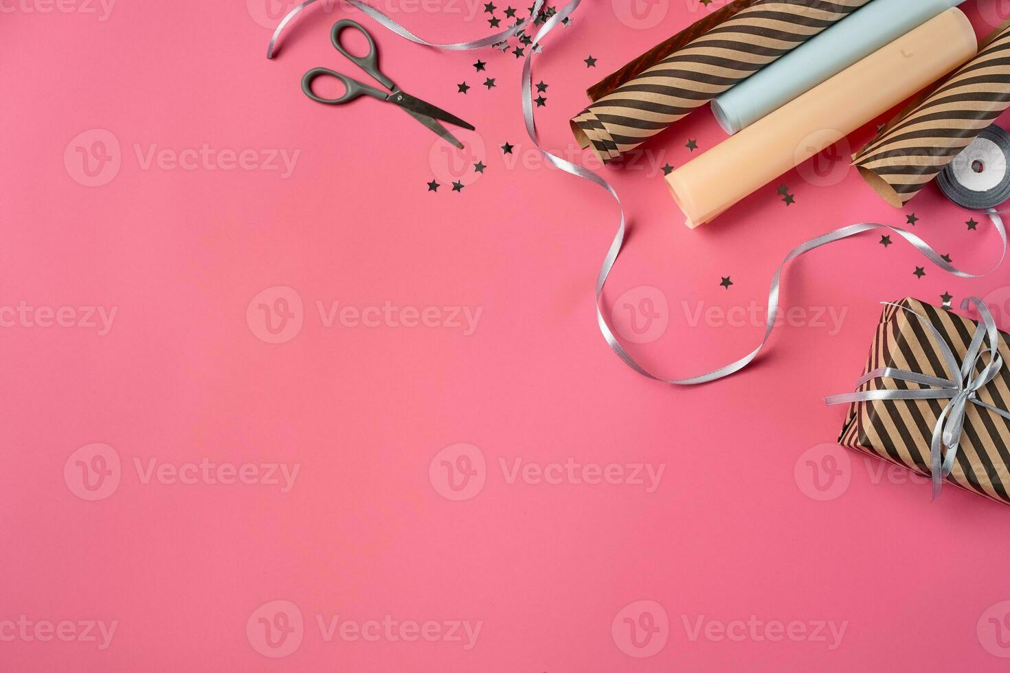 Striped brown gift box tied with silver ribbon on a pink background. Wrapping paper and scissors are laying nearby. Close-up, copy space, top view. photo