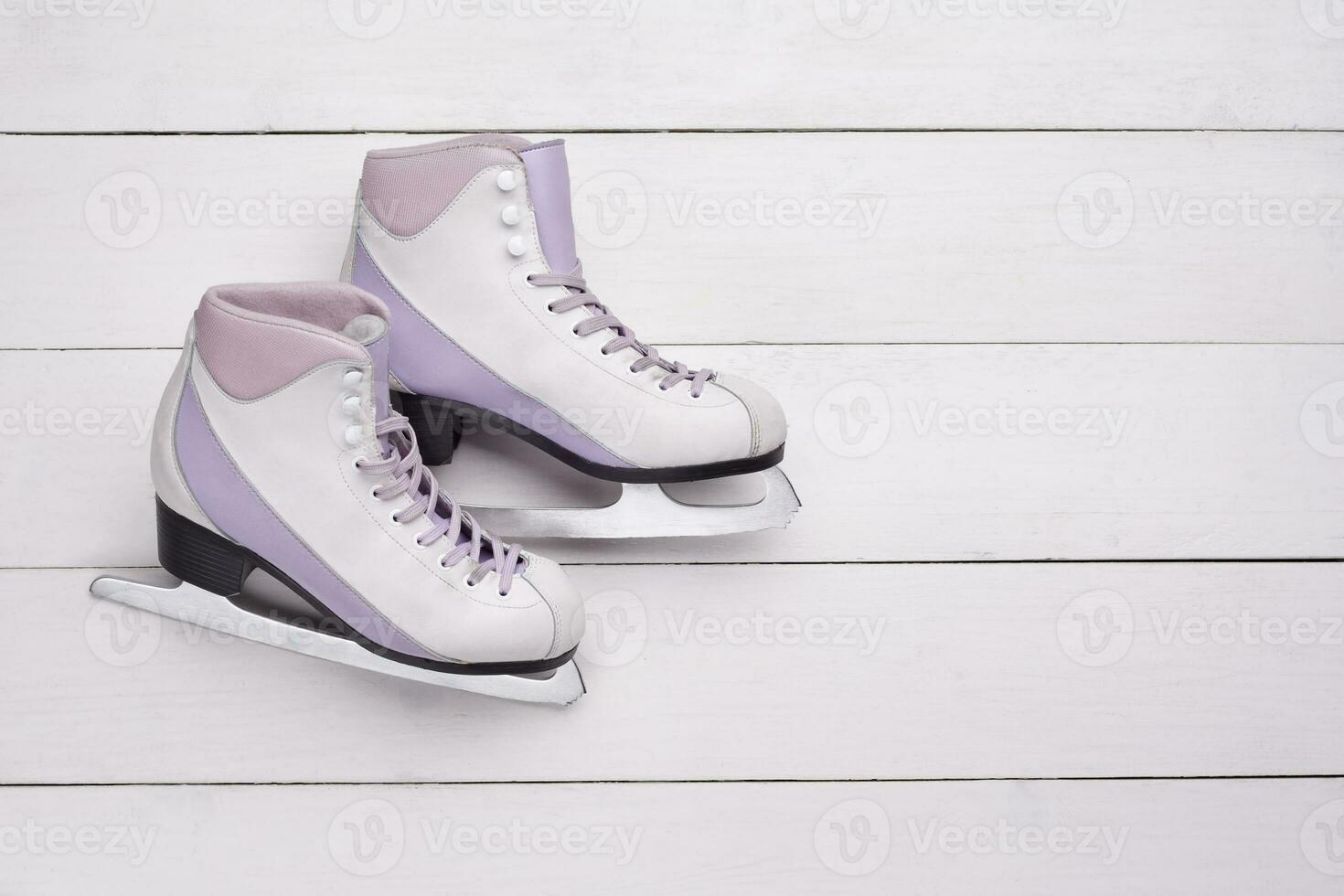 Close-up photo of professional ice skates lying on a white wooden background.