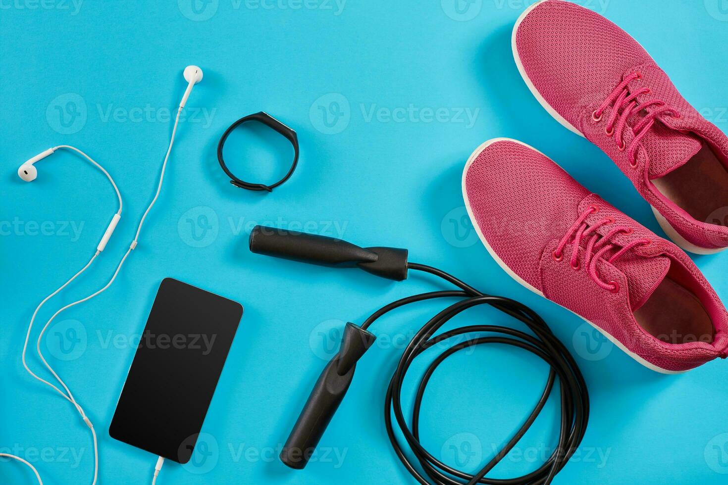 Flat lay shot of Sport equipment. Sneakers, jump rope, earphones and phone on blue background. photo