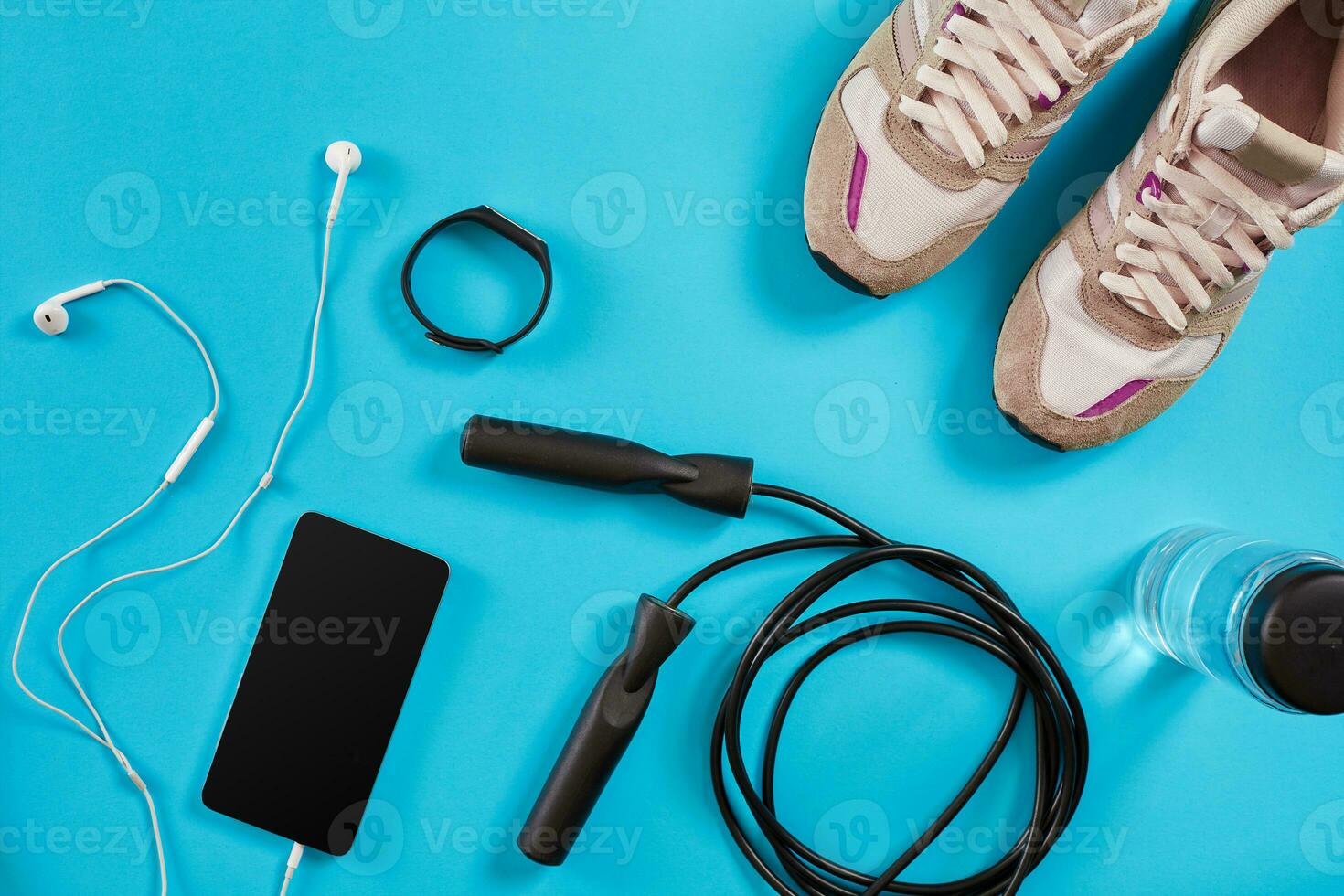 Flat lay shot of Sport equipment. Sneakers, jump rope, earphones and phone on blue background. photo