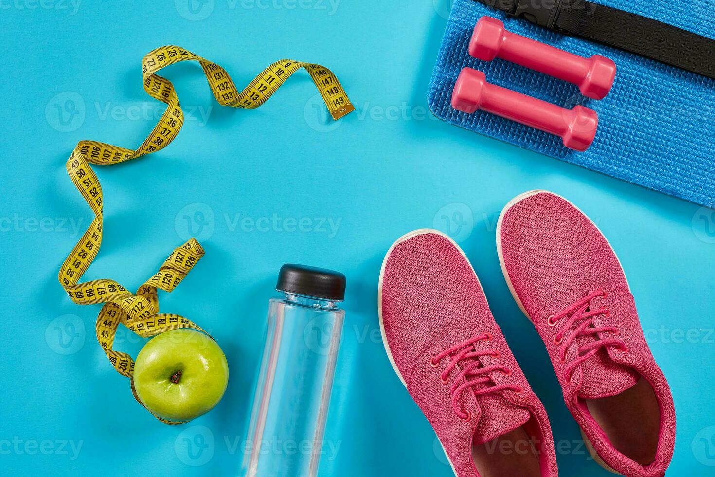 Sneakers with measuring tape on cyan blue background. Centimeter in yellow color, pink sneakers, dumbbells and bottle of water, copy space. photo