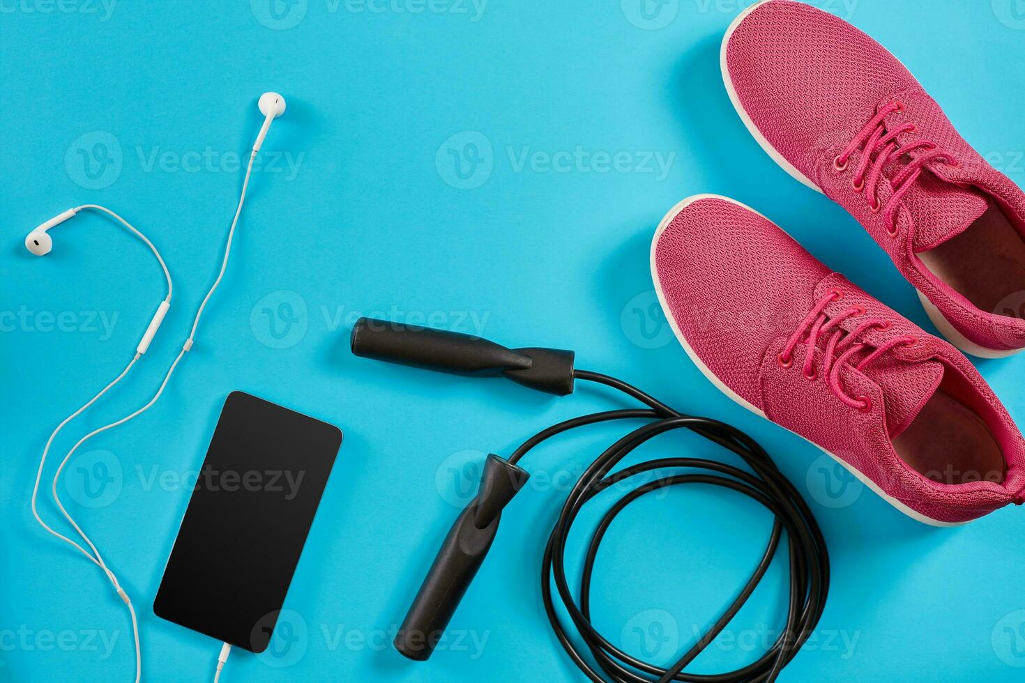 Flat lay shot of Sport equipment. Sneakers, jump rope, earphones and phone on blue background. photo
