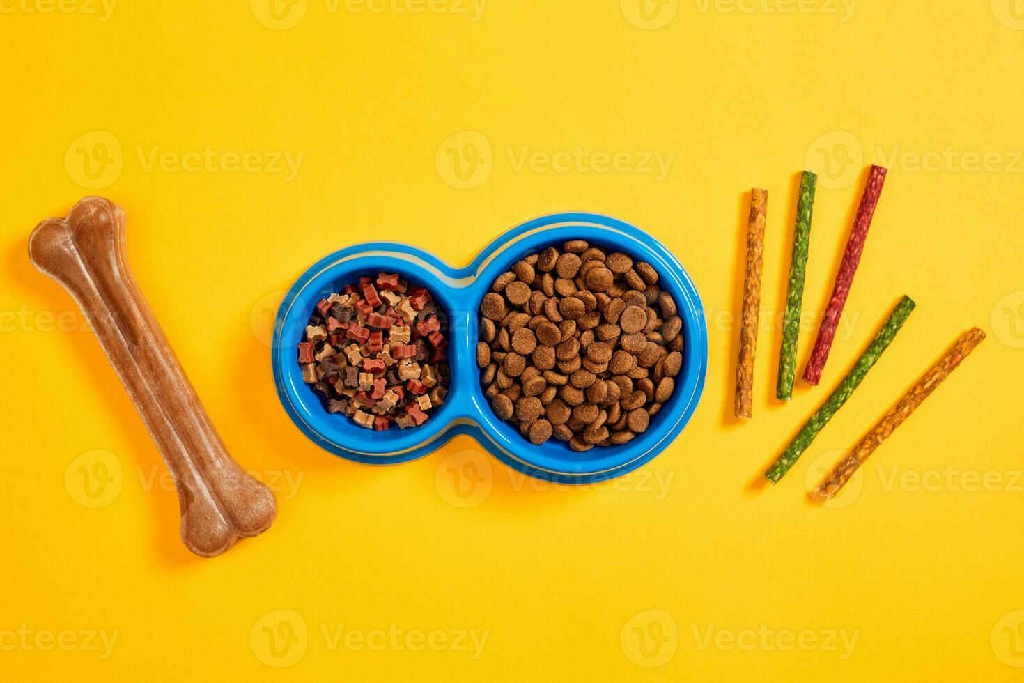 Dog food in blue bowl and accessories on yellow background photo