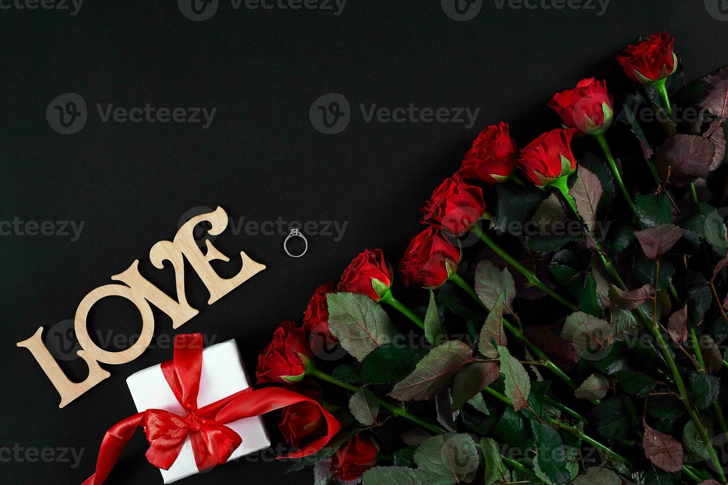 Red roses, ring and gift box on black background photo