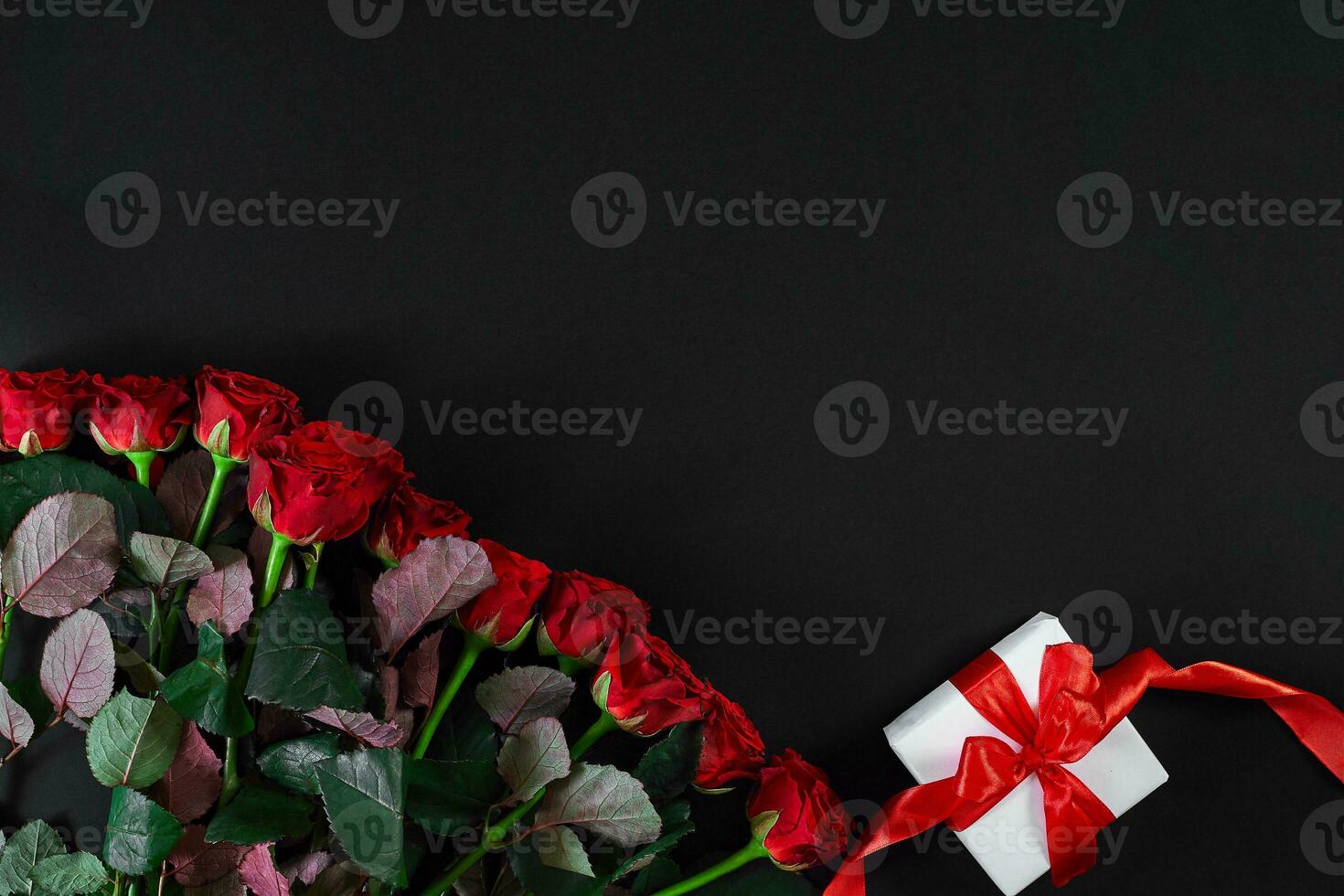 Red roses and white gift box with red ribbon on black background photo