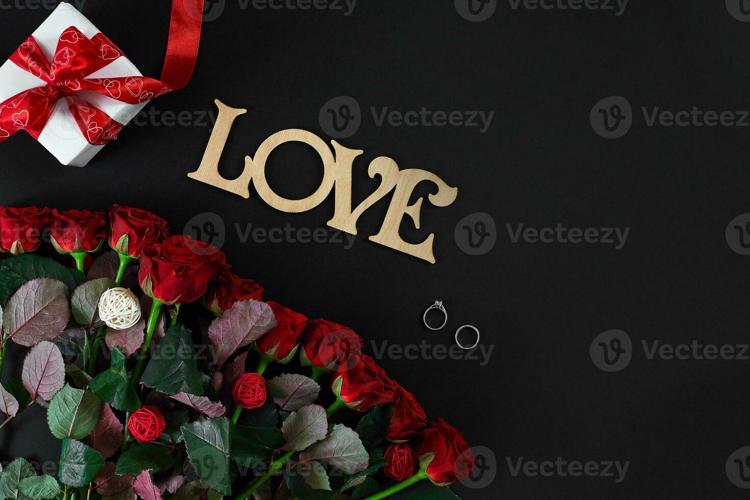 Red roses, ring and gift box on black background photo