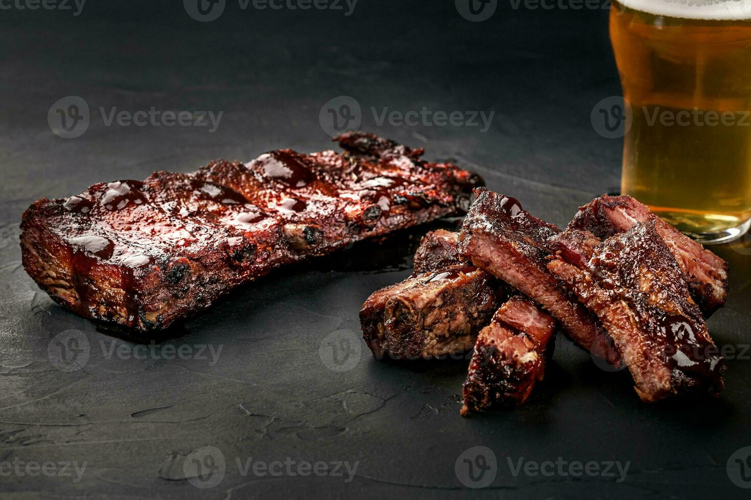 Cerdo costillas en parilla salsa y un vaso de cerveza en un negro pizarra plato. un genial bocadillo a cerveza en un oscuro Roca antecedentes. parte superior ver con Copiar espacio foto