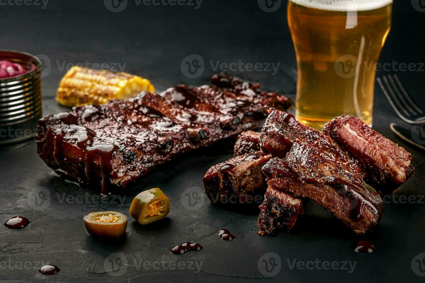 Pork ribs in barbecue sauce and a glass of beer on a black slate dish. A great snack to beer on a dark stone background. Top view with copy space photo